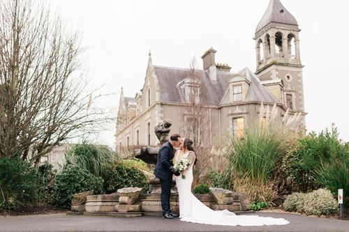 A couple shares an intimate moment in front of a grand Gothic Revival church with ornate architectural details.