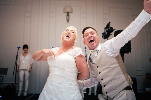 Joyful couple celebrates on the dance floor at their wedding reception, expressing pure excitement and happiness.
