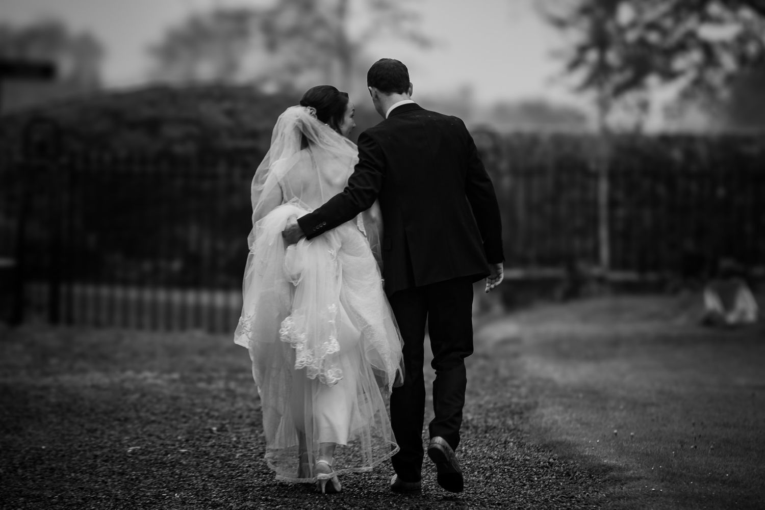 Black and white romantic photo of a couple walking together through a garden.