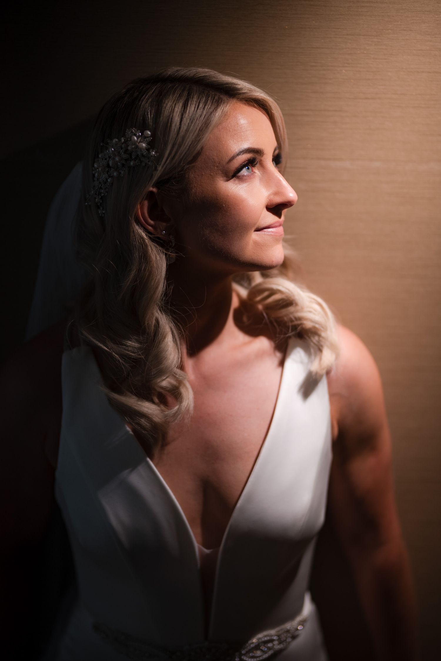 Side profile of a bride in a sleek white wedding dress with soft waves and delicate hair accessories.