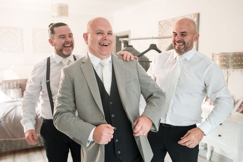 Three men in formal attire laughing together in a bright indoor setting.