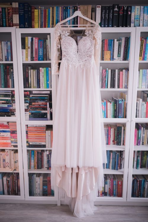 White lace wedding dresses hanging from built-in bookshelves filled with colorful books.