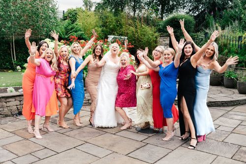 Wedding party celebrating on a stone patio with their arms raised in joyful celebration.