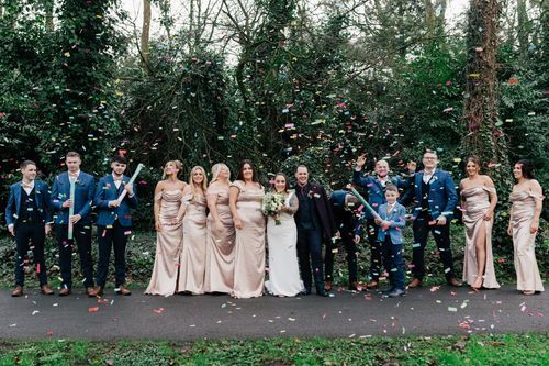 Wedding party stands together on a forest path while confetti falls around them during outdoor celebration.