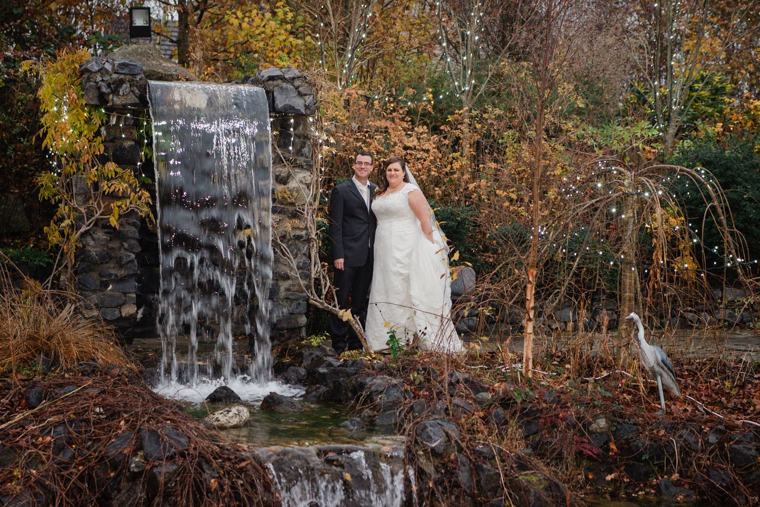 Romantic wedding portrait by a waterfall with autumn foliage in the background.