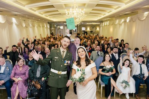 A joyful wedding celebration with the newlyweds and guests in an elegant ballroom with crystal chandeliers.
