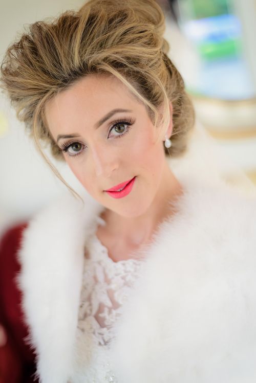 Close up portrait with soft makeup, blonde updo hairstyle, red lipstick, white fur wrap and lace dress details.