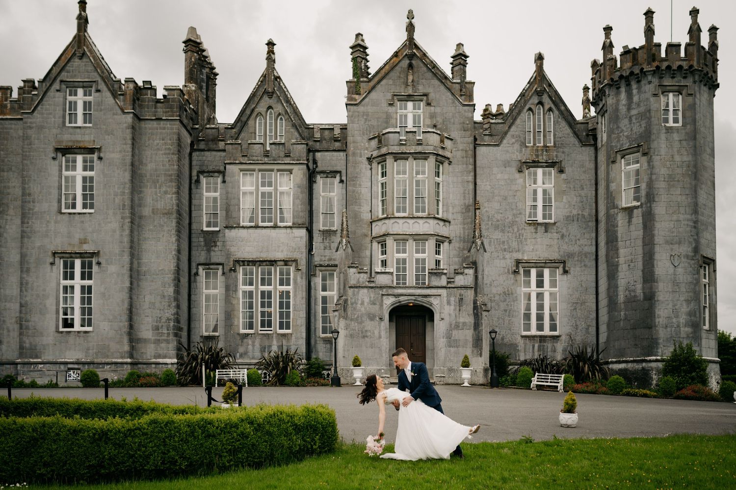 Bride and groom share a romantic dip kiss in front of a grand Irish castle on their wedding day.