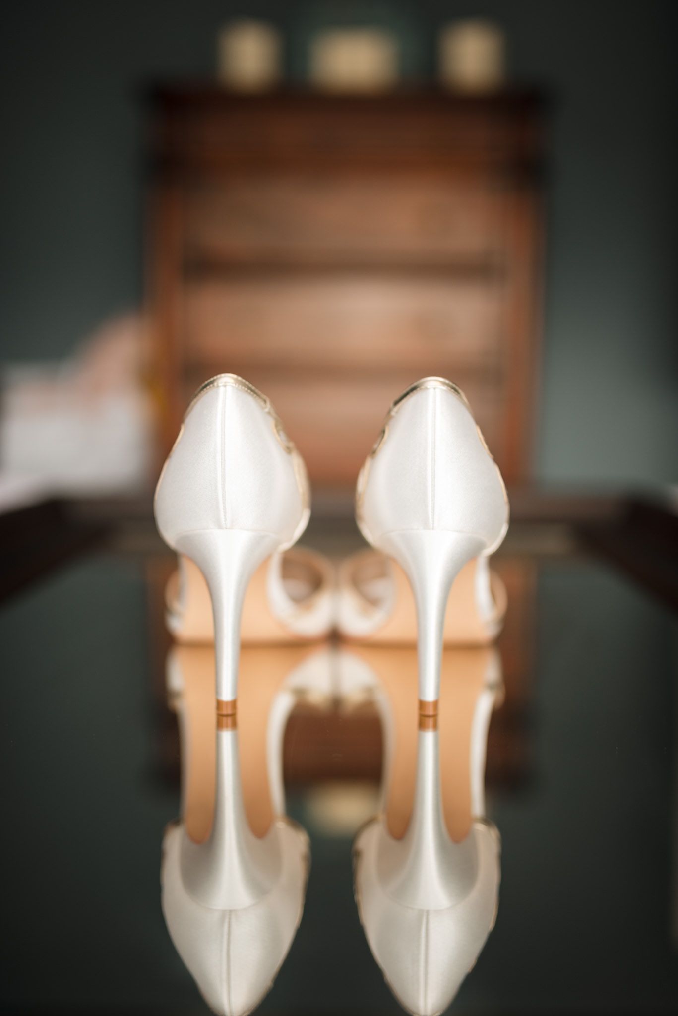Elegant white bridal heels photographed with shallow depth of field against dark background.