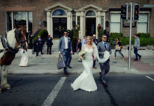 A wedding couple dances together during their first dance on an outdoor patio surrounded by guests and brick buildings.