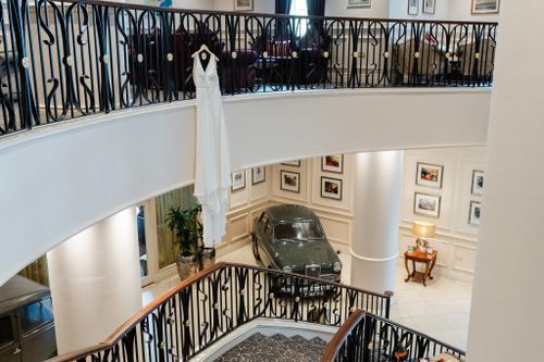 Vintage car displayed in elegant museum interior with curved staircase and black wrought iron railings.