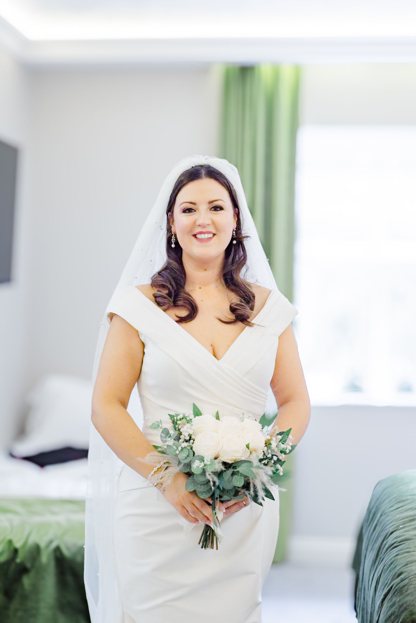 Radiant bride in white V-neck wedding dress holding eucalyptus and rose bouquet.