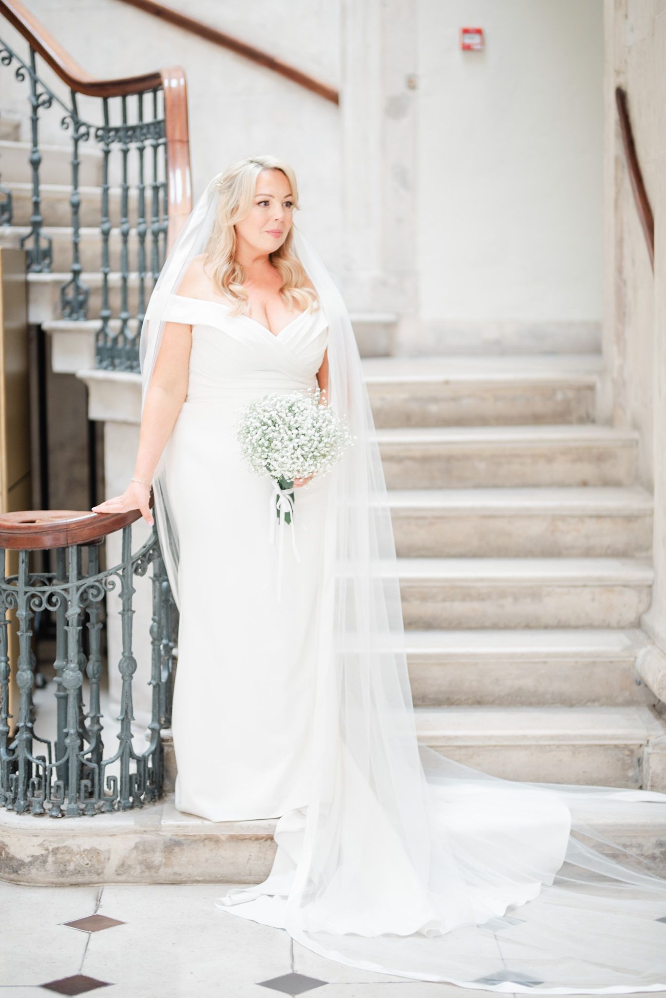 Elegant wedding portrait on stone staircase with flowing veil and baby's breath bouquet.