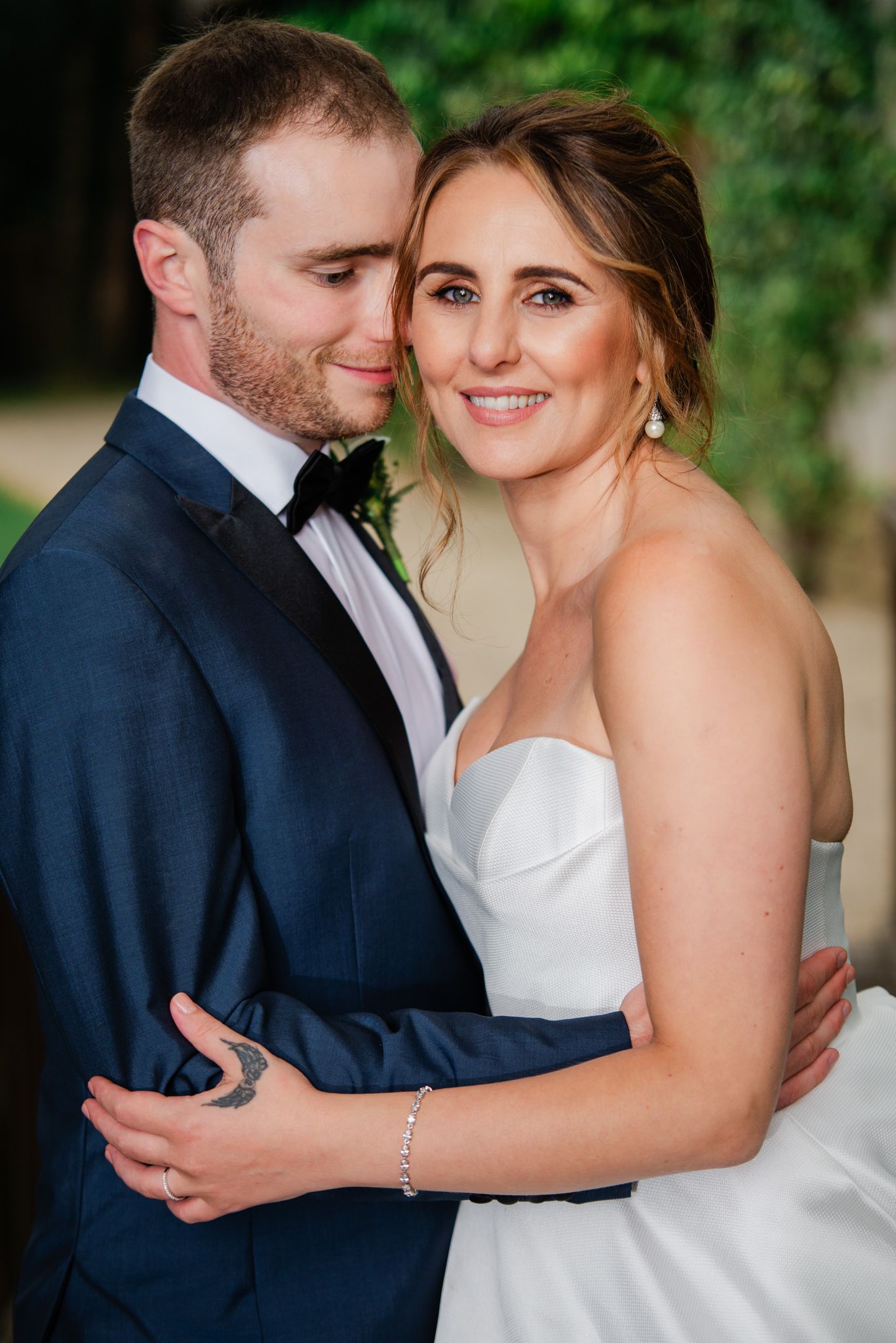 A romantic wedding portrait features a couple embracing outdoors with the bride in white and groom in navy.