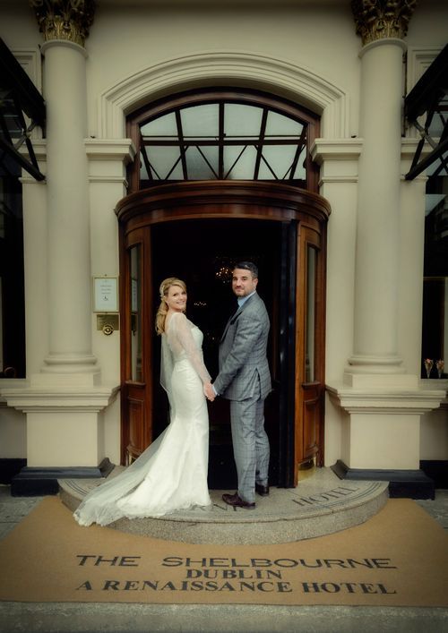 A couple poses in their wedding attire at the entrance of The Shelbourne Renaissance Hotel in Dublin.