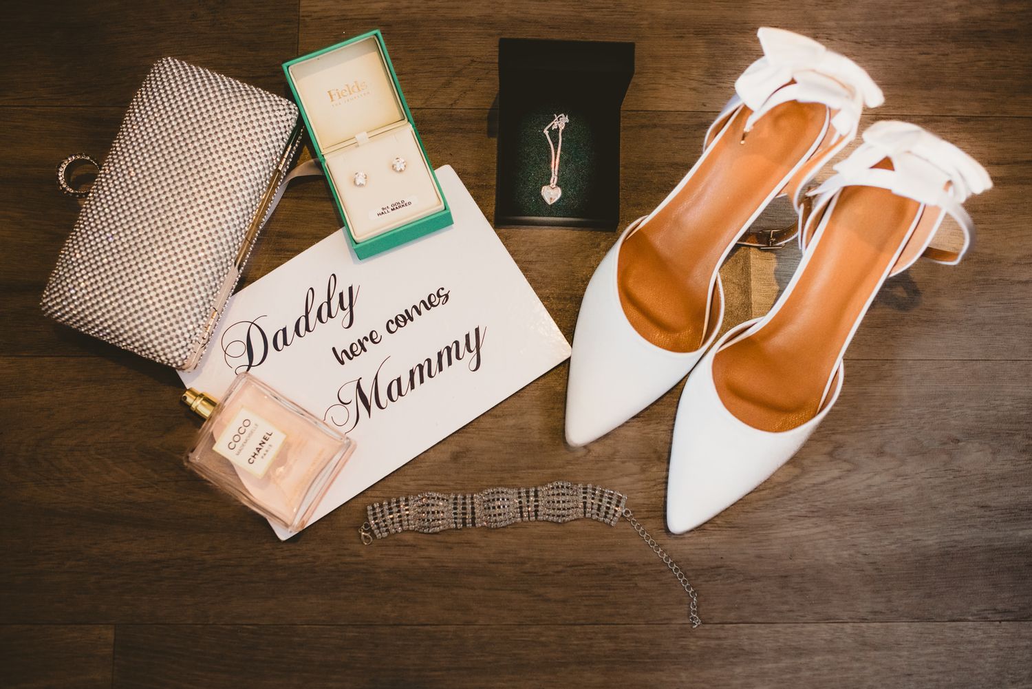Wedding accessories including white shoes, clutch and personalized name cards laid on wooden surface.