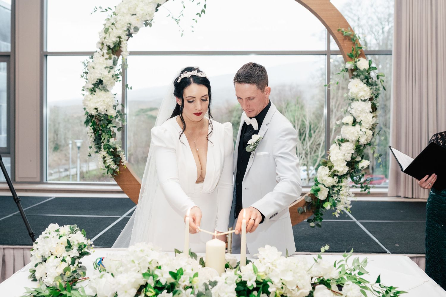A romantic wedding scene with floral decor featuring white and cream roses on an arch and elegant table settings.