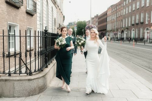 A bridal party in dark green and white dresses walks along a classic Dublin street with historic buildings in the background.