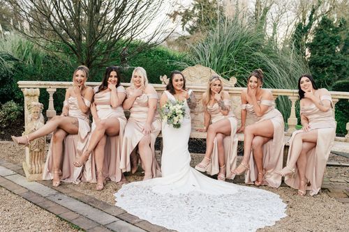 Wedding party in blush pink dresses poses together on stone steps in an elegant garden setting.