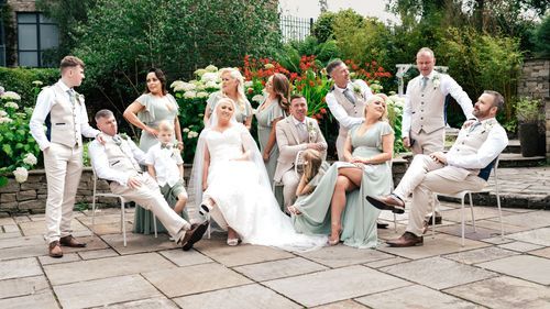 Wedding party in light colored attire relaxing on outdoor patio furniture during sunny garden celebration.