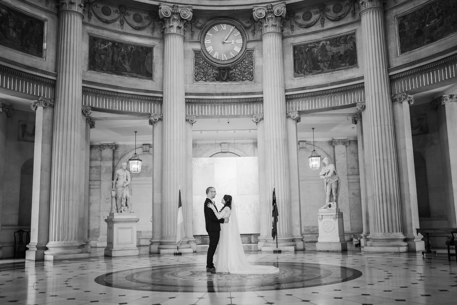 A couple dancing in a grand circular hall with ornate columns and classical architecture.