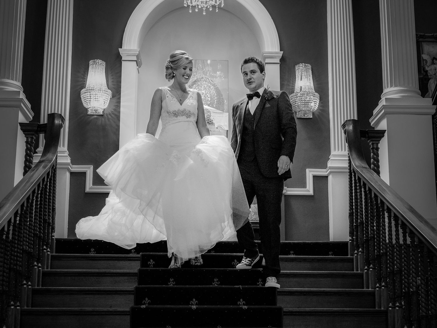 Elegant black and white photo of a couple descending grand staircase with ornate architectural details.