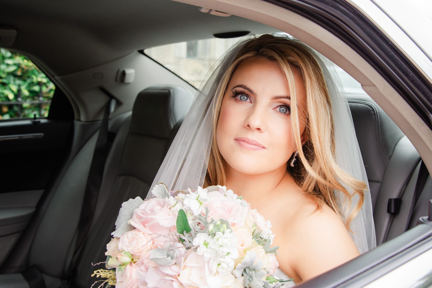 A bridal portrait showing a bouquet of pink flowers inside a car.