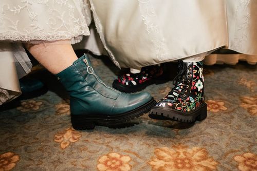 Two pairs of contrasting boots shown side by side - one in teal leather and one in floral print pattern on patterned carpet.