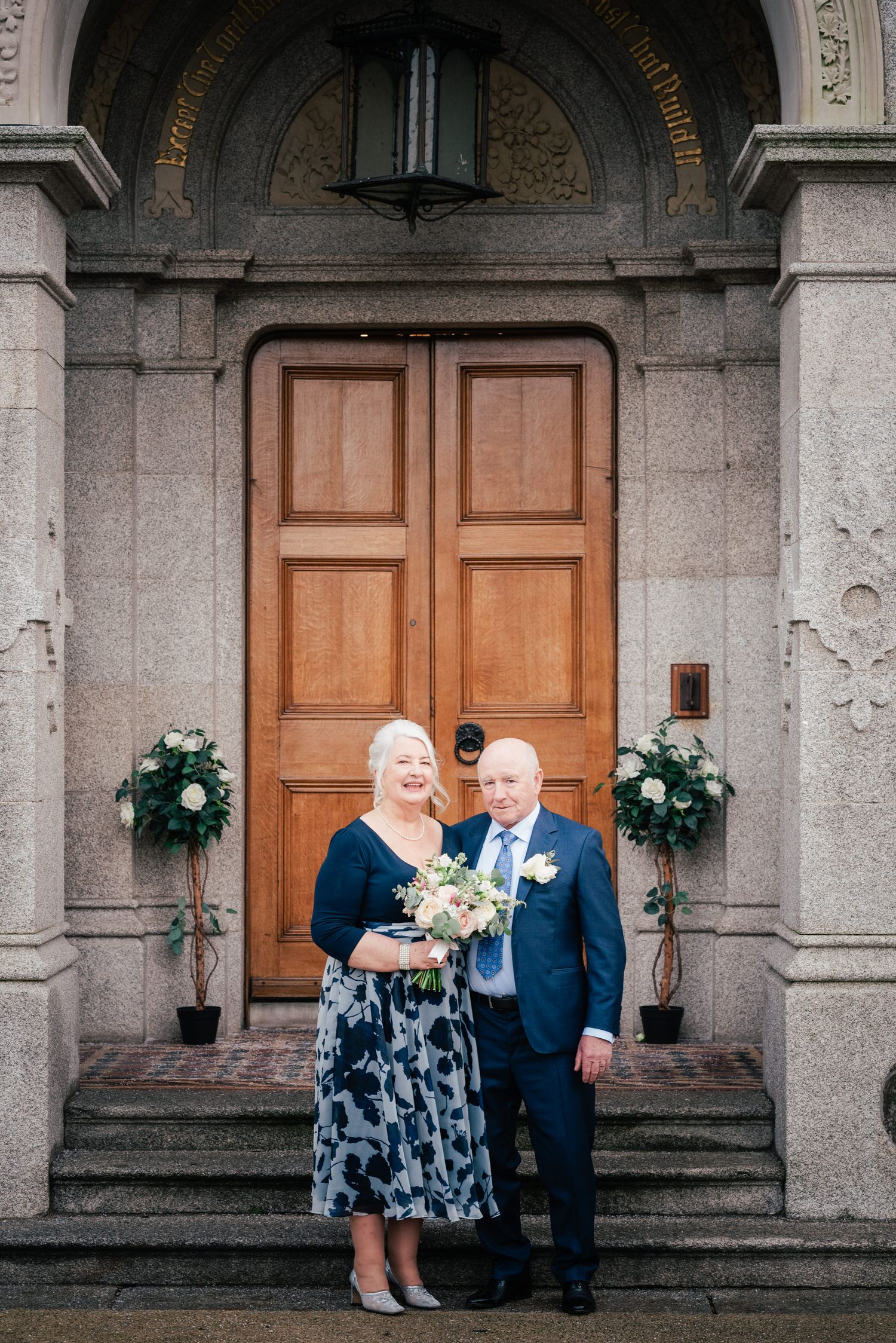 Elegant church entrance with wooden doors, stone archway and decorative floral arrangements on the steps.