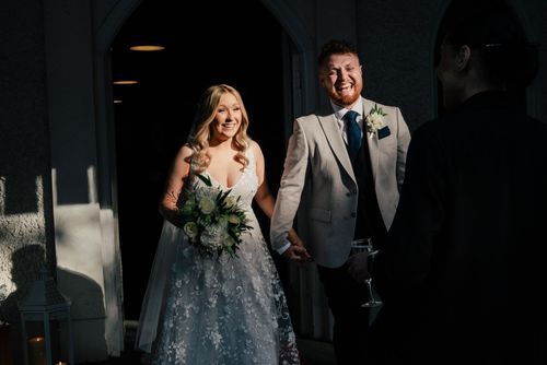 A happy bridal couple walking together, the bride wearing a sparkly blue and white gown while holding a green bouquet.
