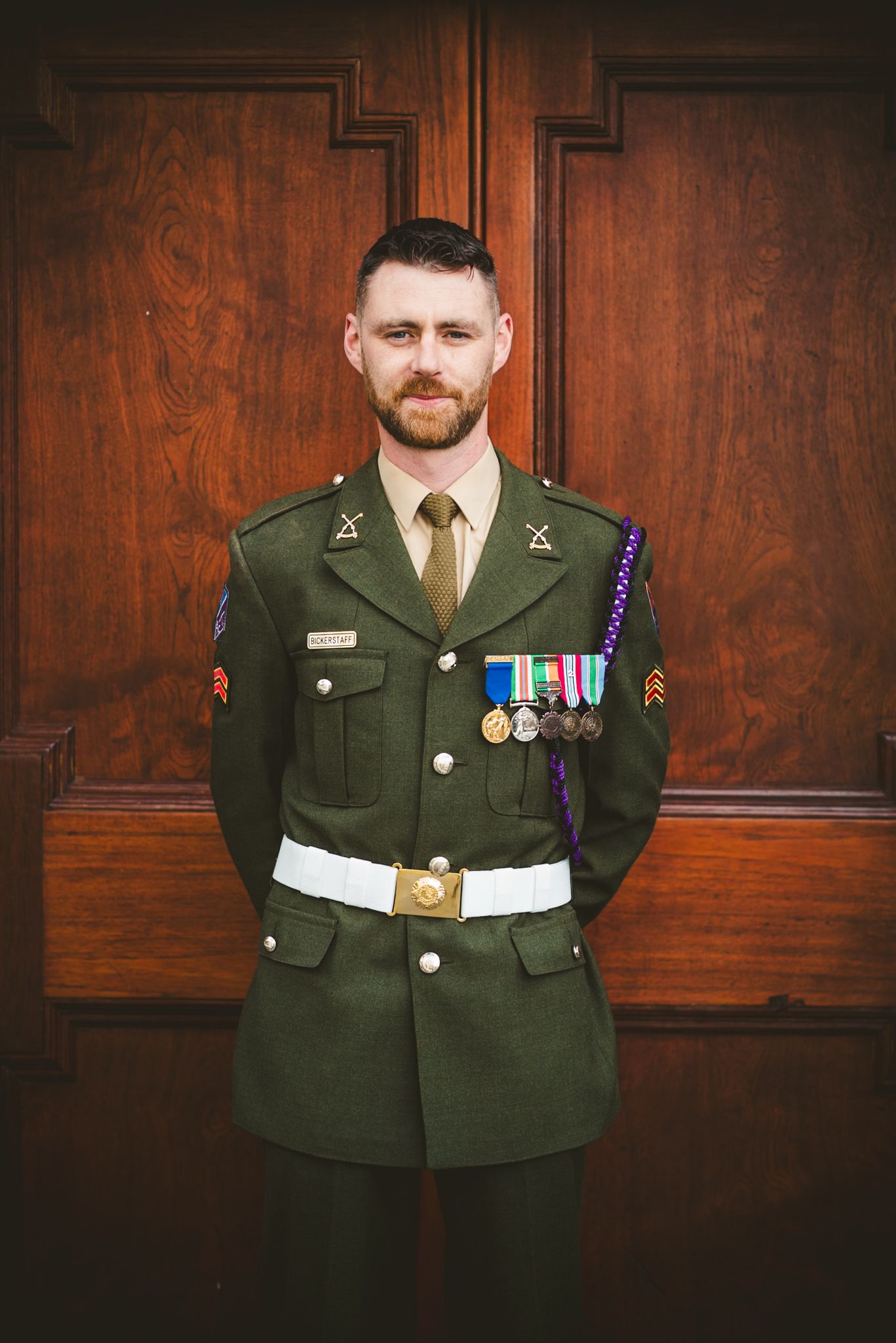 Military serviceman in formal dress uniform with medals standing in front of wooden doors.