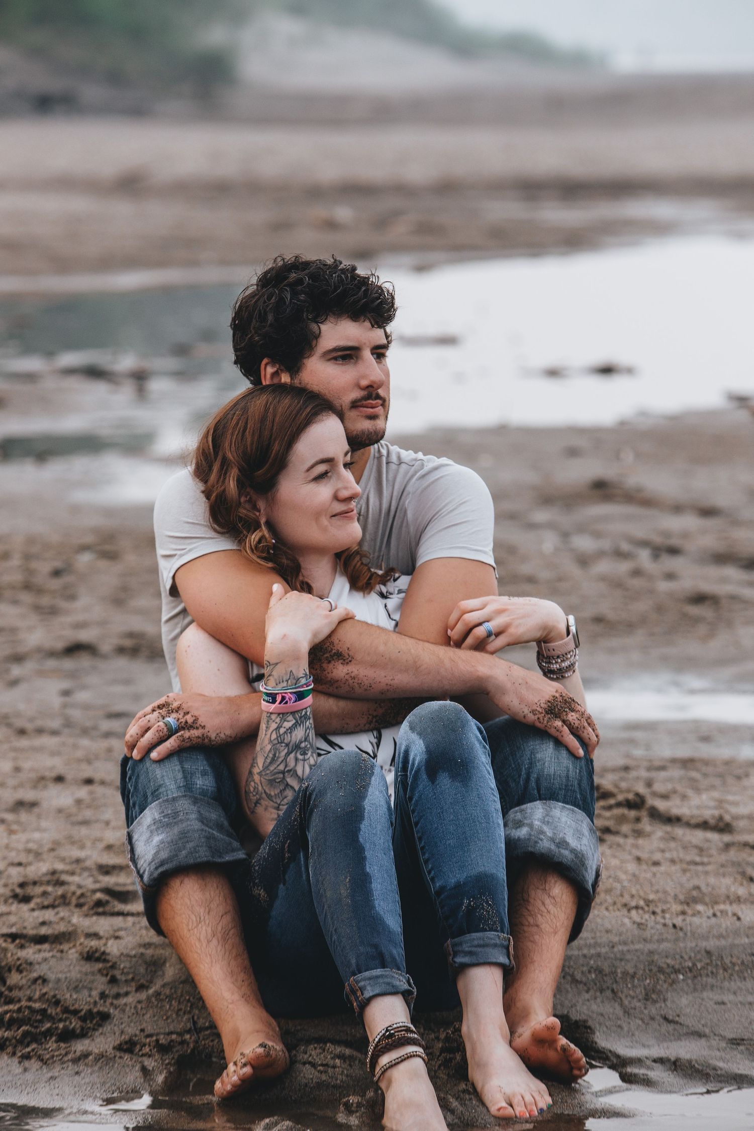 A couple sits close together on a sandy beach, sharing intimate moments in a series of casual poses.