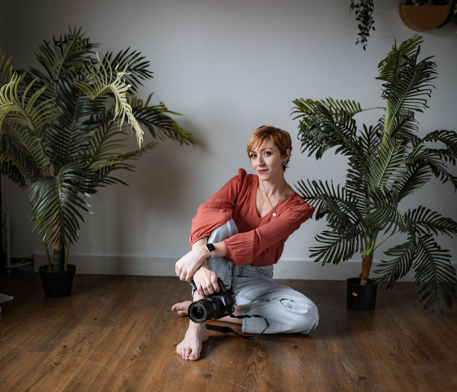 Indoor photography scene with tropical plants showing photographer sitting cross-legged with camera.