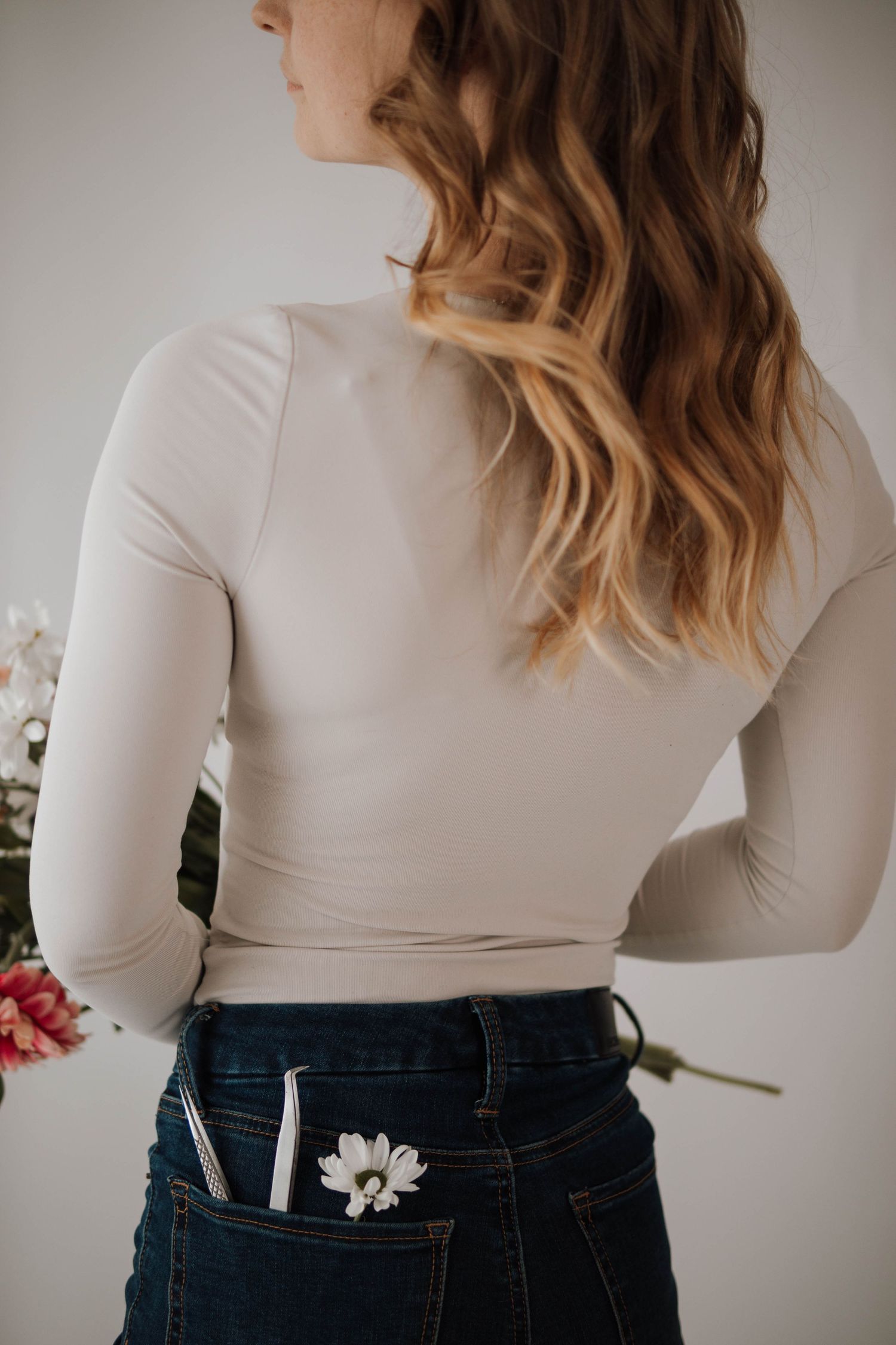 Back view of someone wearing a white top and jeans with a flower tucked in the back pocket.