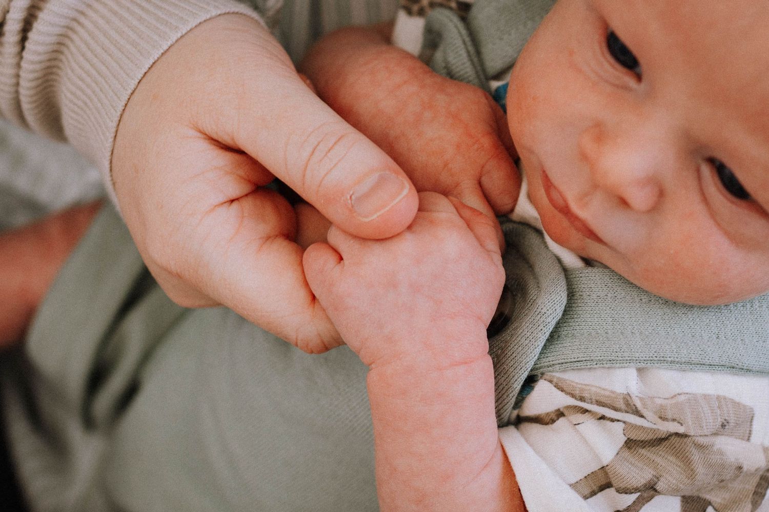 Close-up of a tiny newborn baby's hand being held gently by an adult finger.