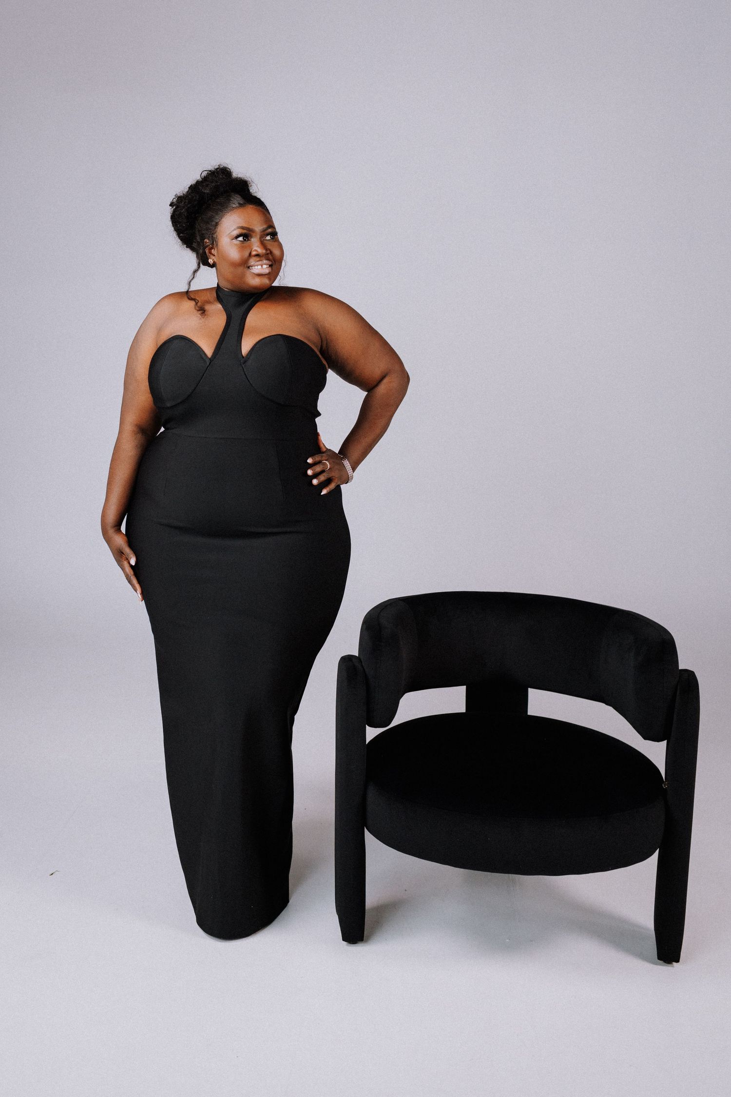 A series of artistic photographs showing a person in a black dress posing with a curved modern chair against a gray backdrop.