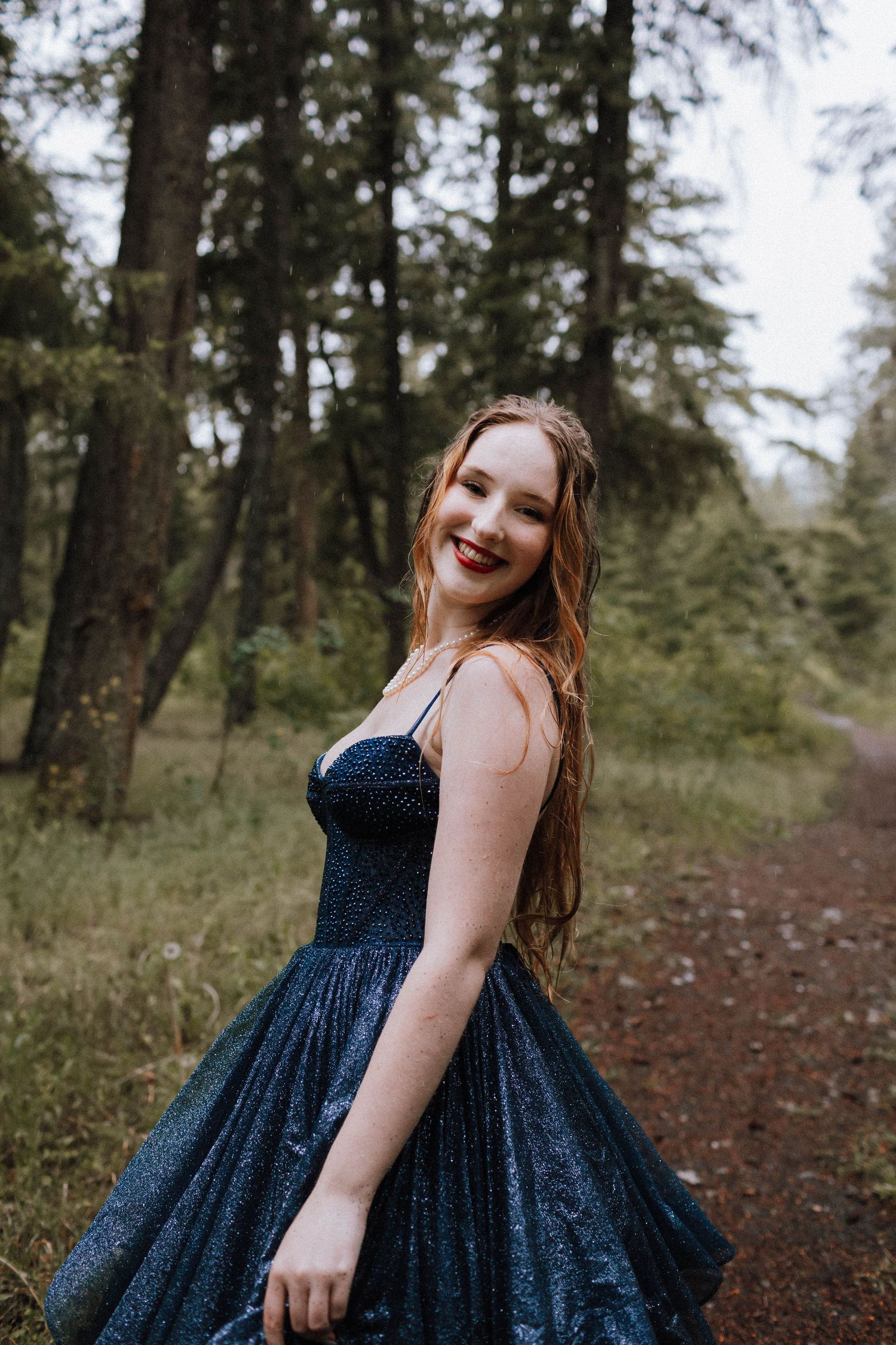 A glittering navy blue ballgown captures the sunlight on a forest trail.