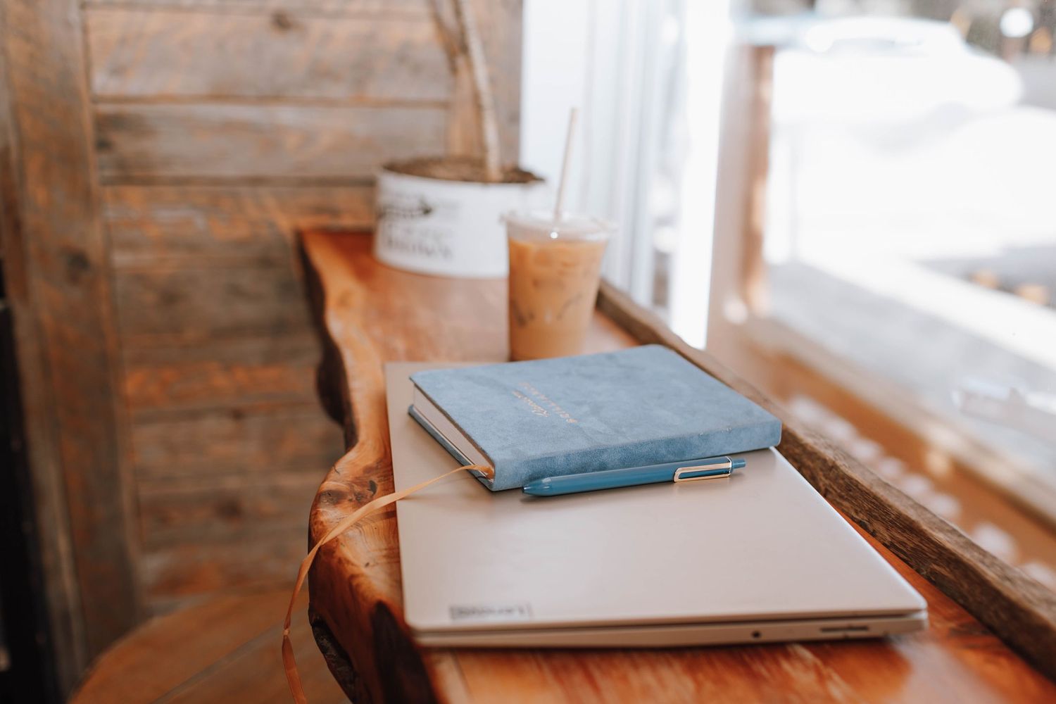 Blue notebook and papers arranged on a rustic wooden table with coffee cups.