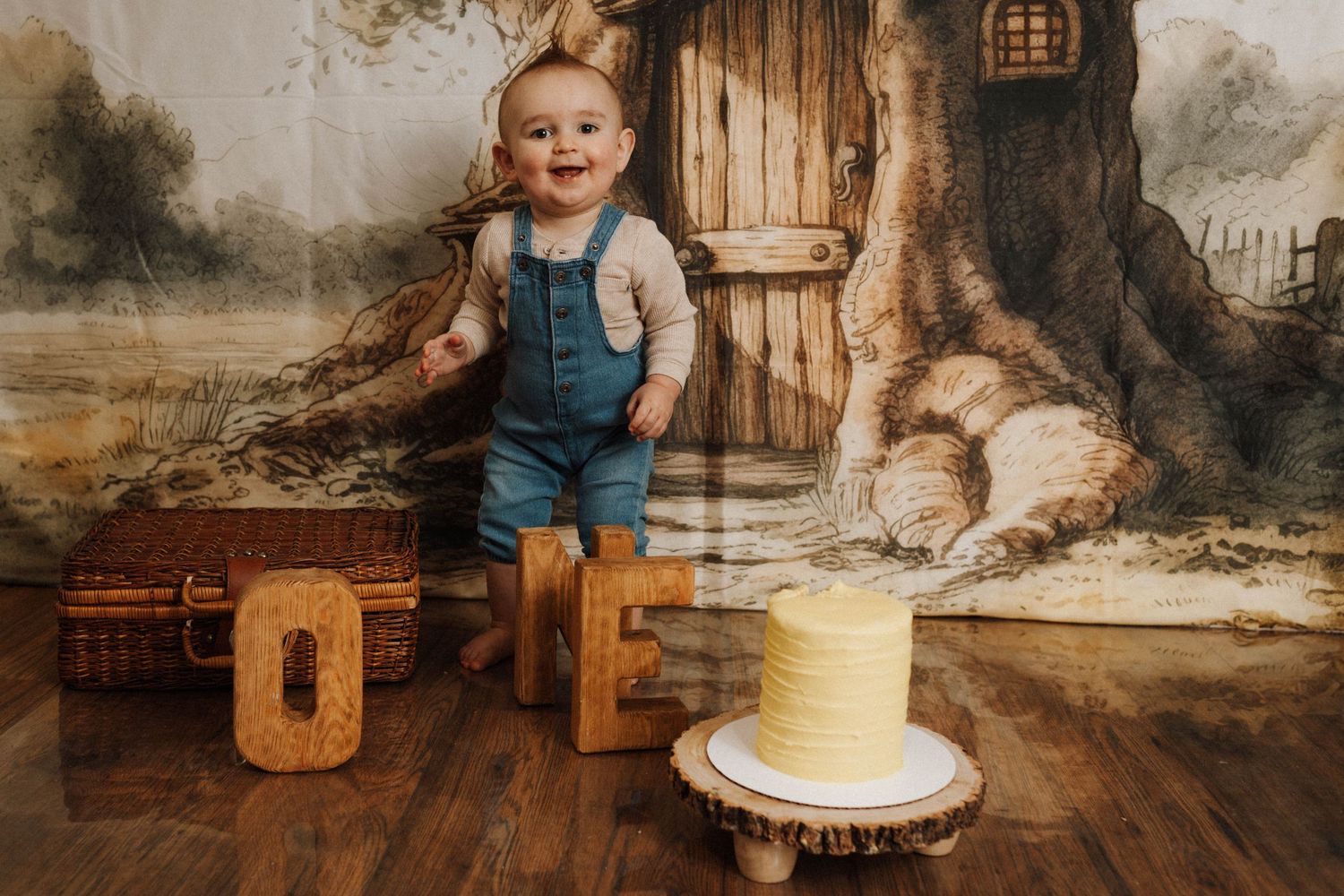 Whimsical first birthday setup with wooden letters and cake against fairy tale tree backdrop.