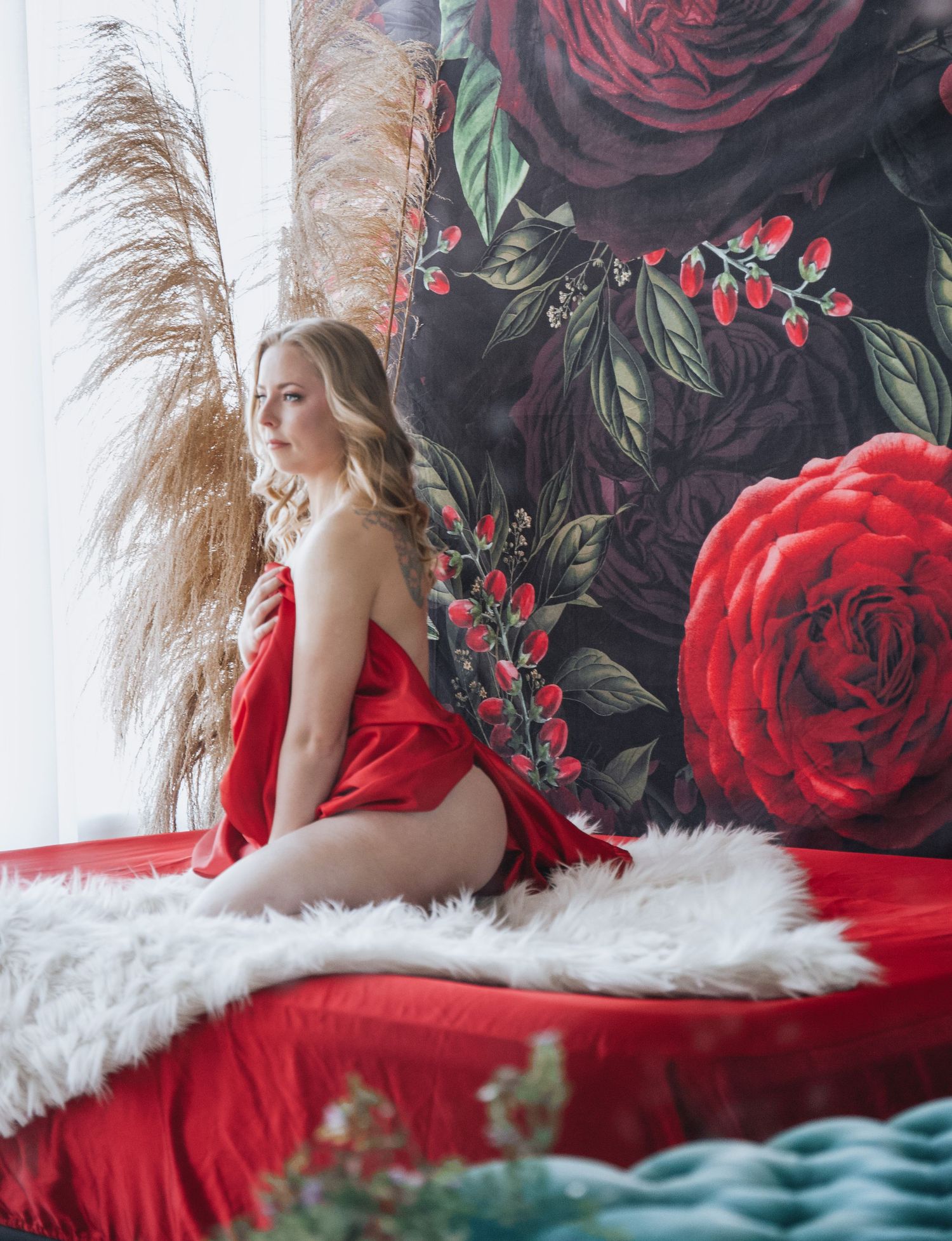 Elegant boudoir photo with red roses and pampas grass against floral wallpaper.