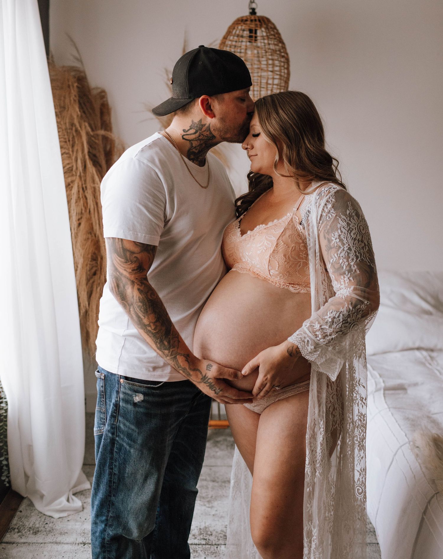 A tender maternity moment captured in front of woven decor and sheer curtains.