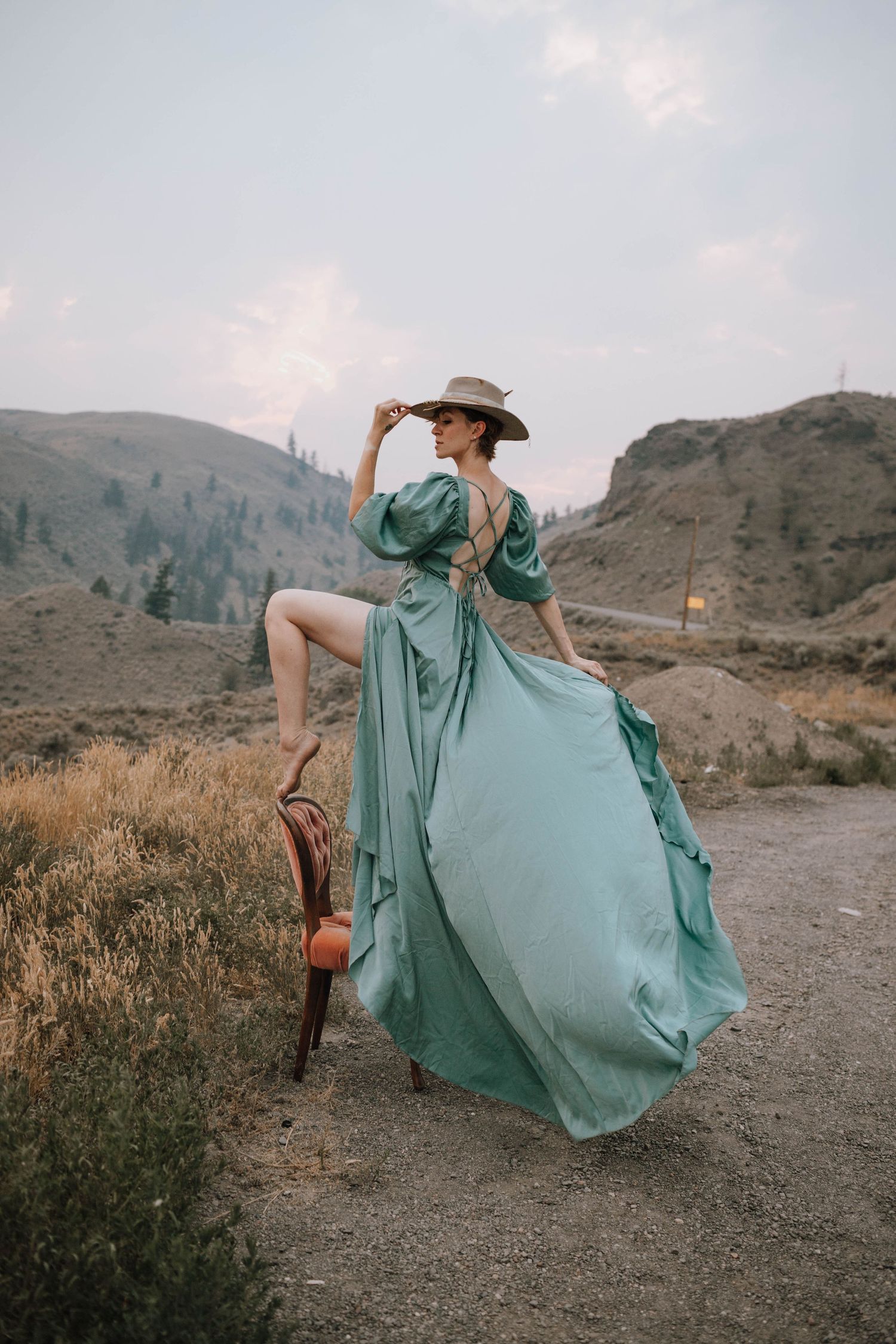 Flowing teal dress catches wind on mountain path during golden hour photoshoot.