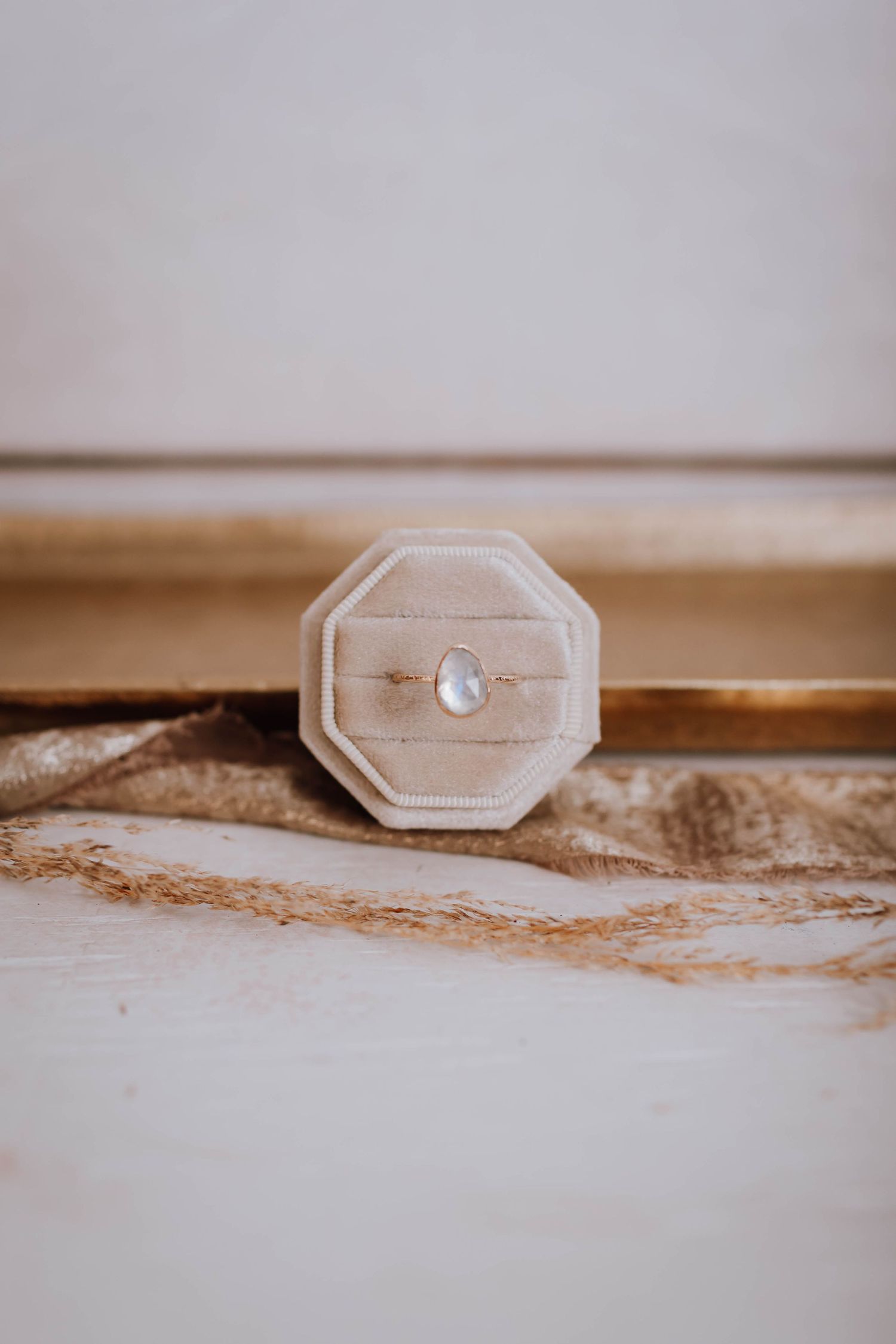 Elegant octagonal ring box with delicate ring on textured neutral background.
