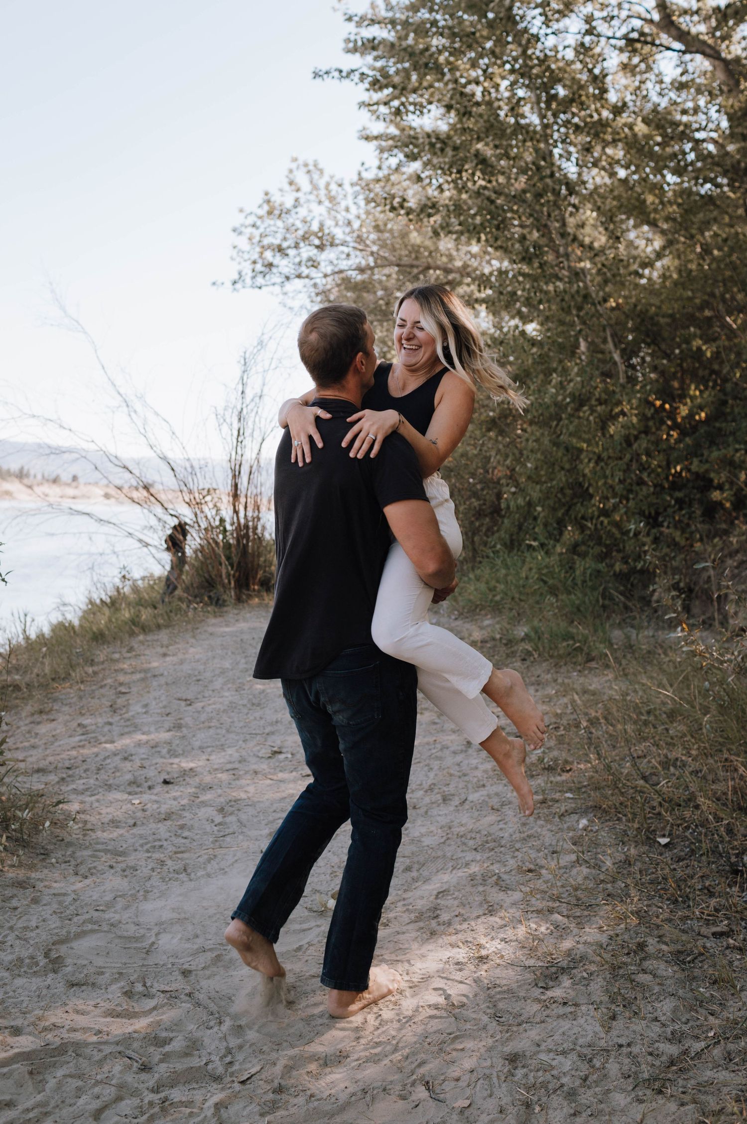 A couple shares a joyful moment with a fun lift pose on a natural path.
