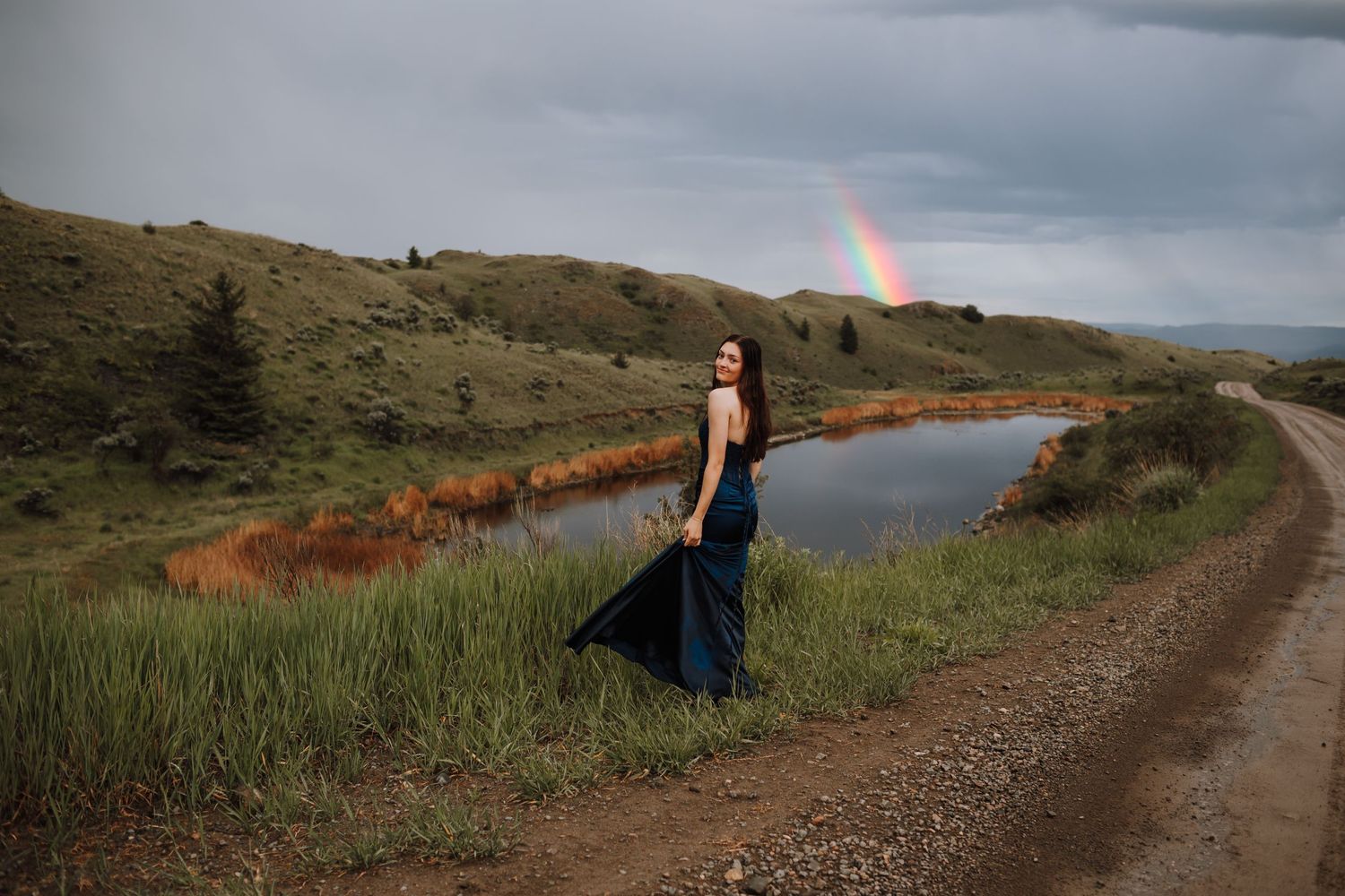 A navy dress silhouetted against stormy skies with a rainbow visible over mountains.