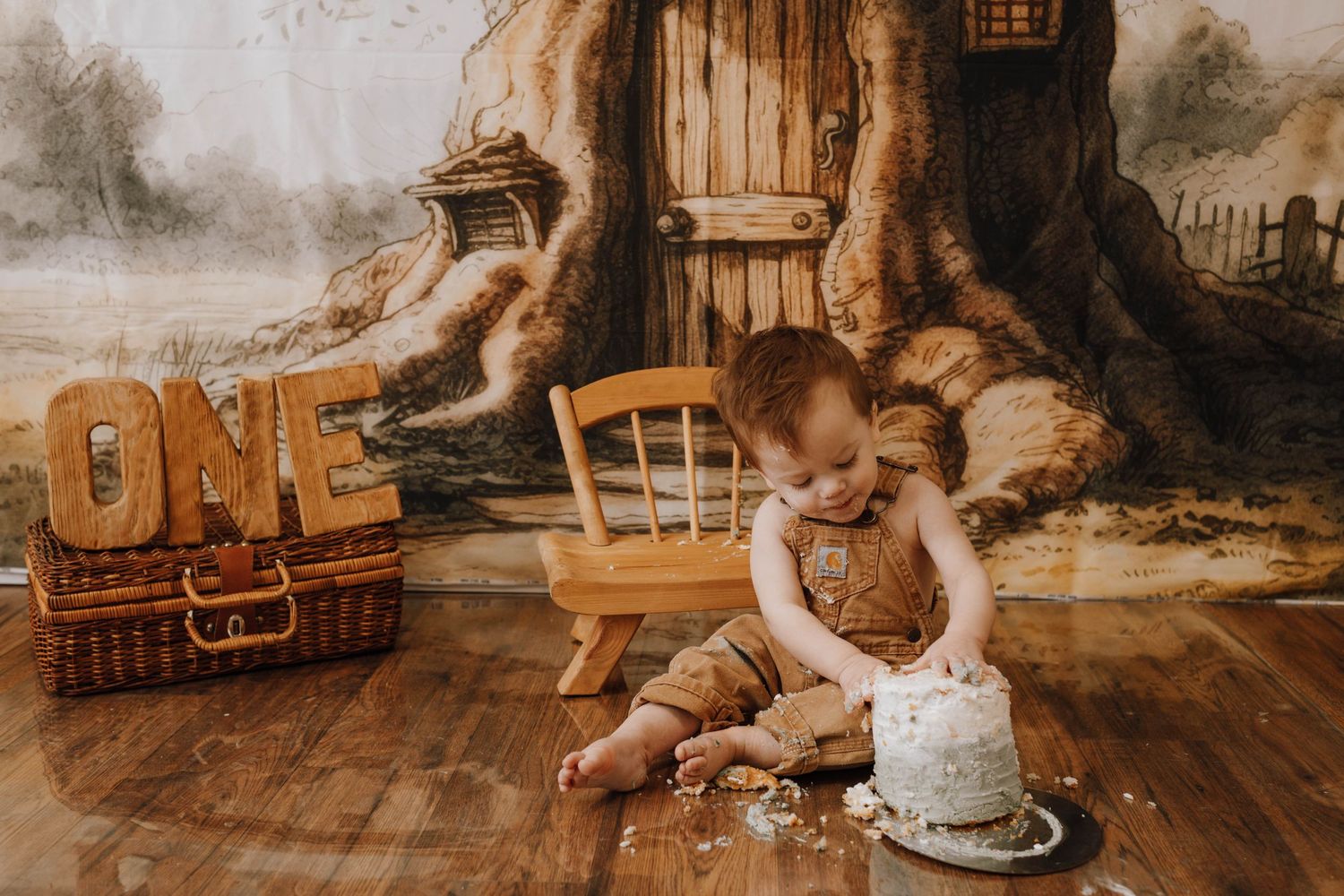 First birthday setup with baby, smash cake, and rustic wooden decorations.