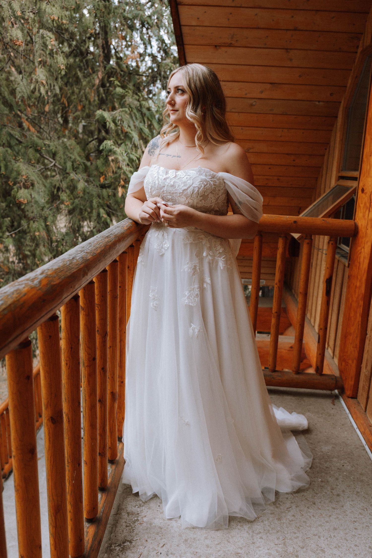 A wedding dress is showcased on a rustic wooden cabin porch with evergreen trees in the background.