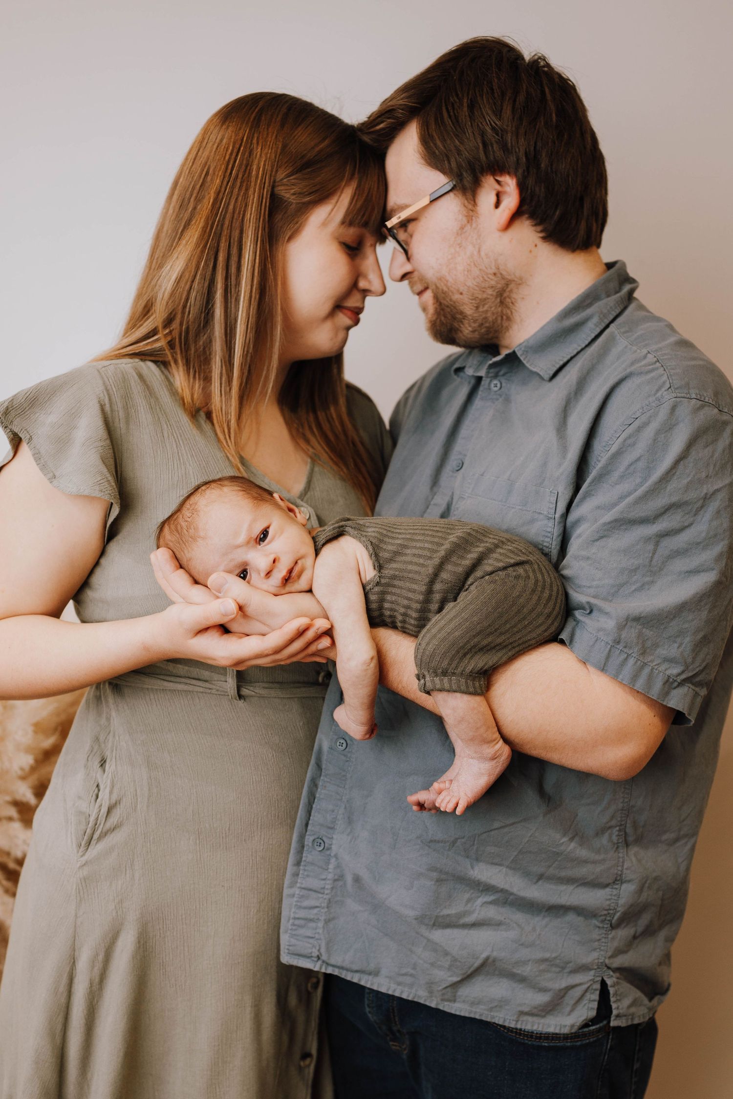 A loving couple holding their newborn baby together in a tender moment against a neutral background.