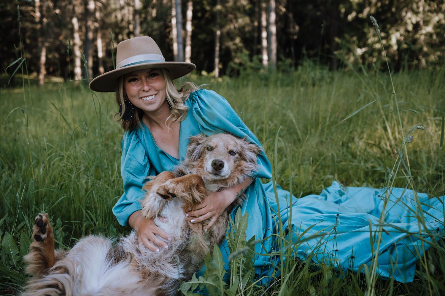 A happy fluffy dog with their owner in a turquoise dress sitting in a grassy meadow on a sunny day.