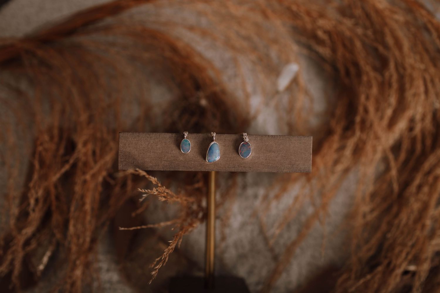 Three small jewelry pieces mounted on a wooden display stand with textured natural fiber background.